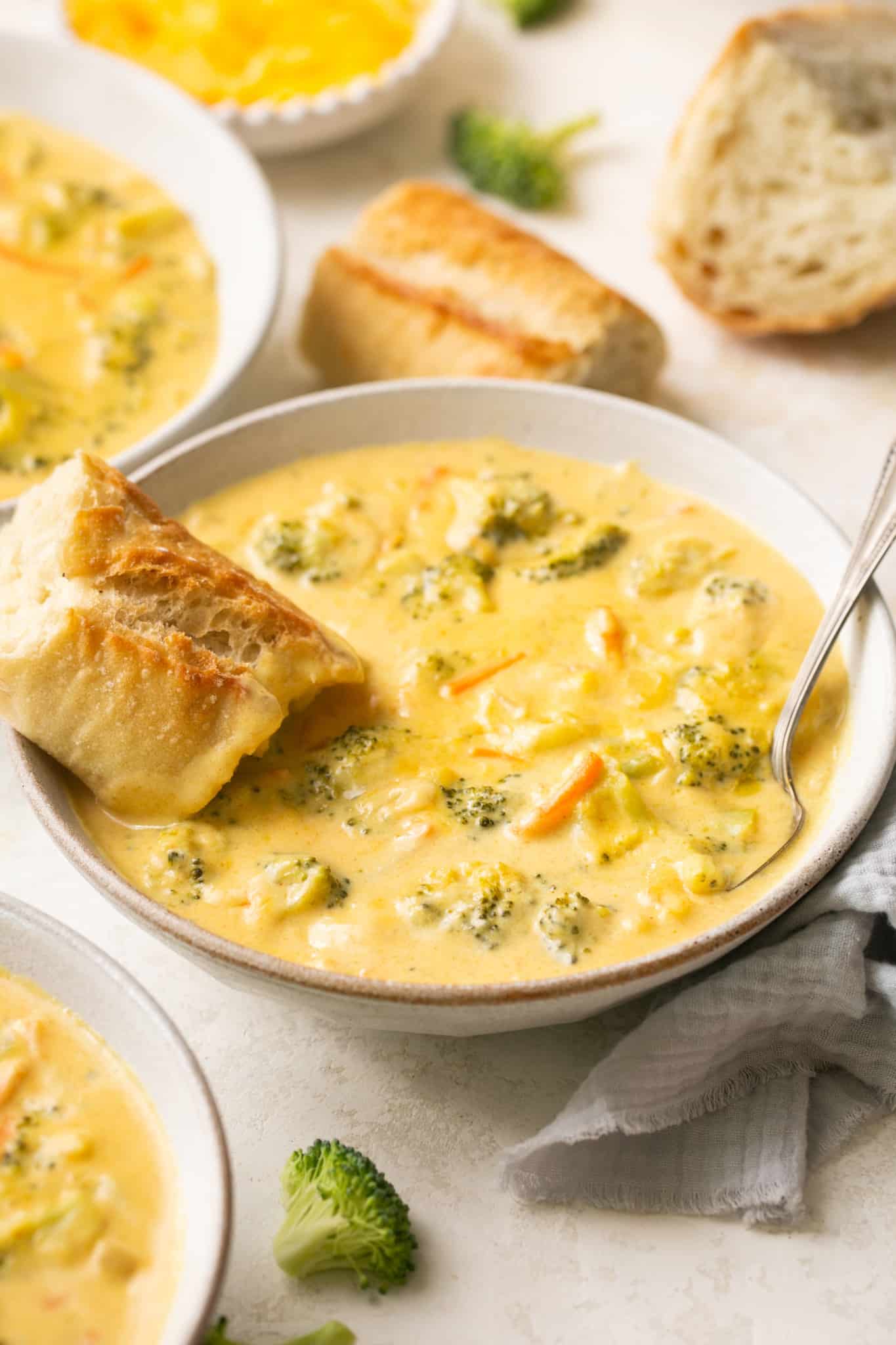 broccoli cheddar soup in a white soup bowl with bread dipping in it. 