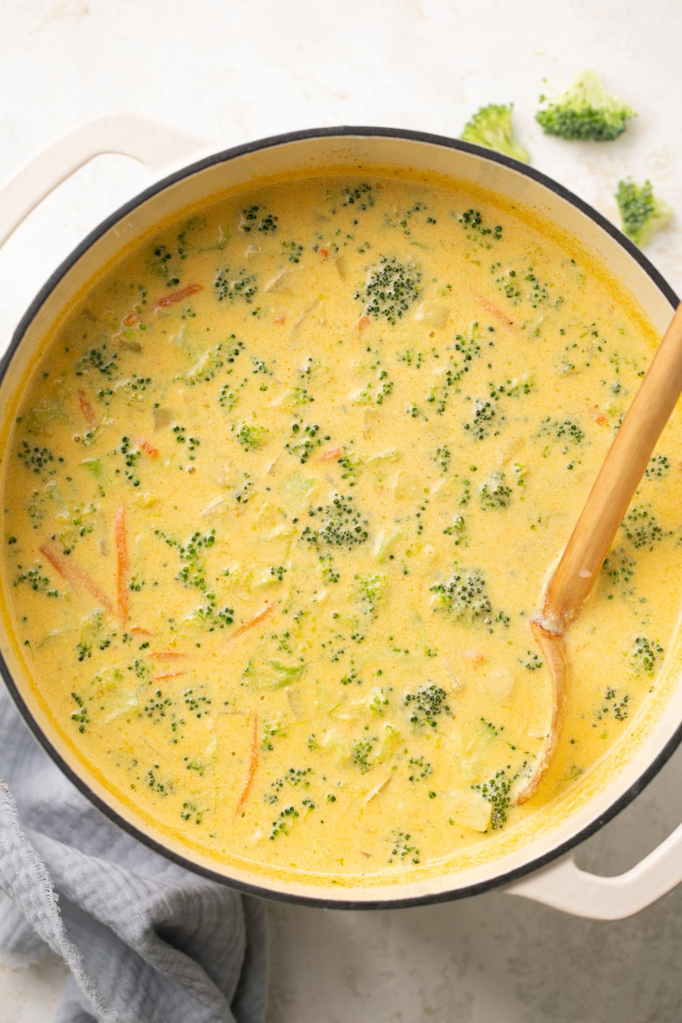 soup made with cheddar cheese and broccoli in a large soup pot with a wooden spoon in it. 