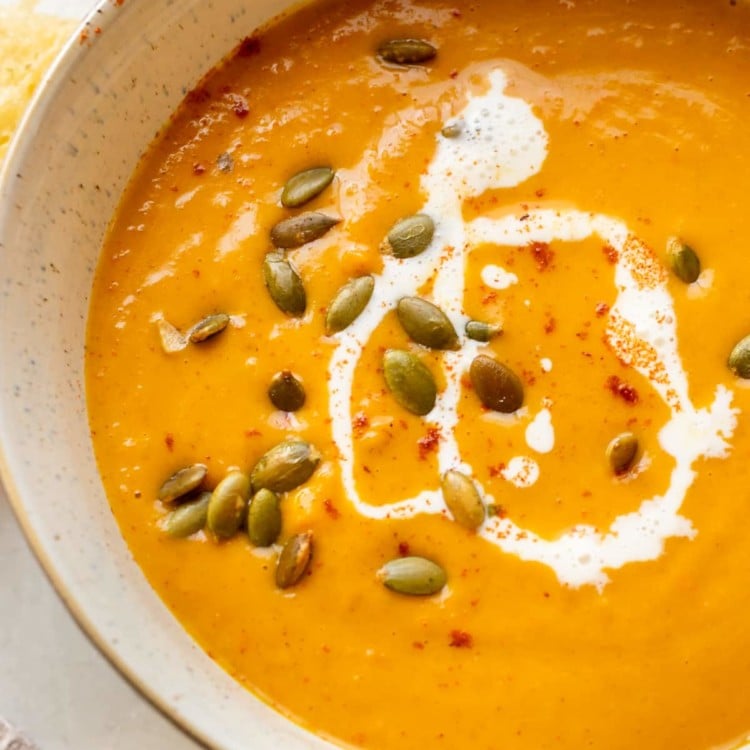 squash soup in a bowl topped with pepitas, cream, and paprika.