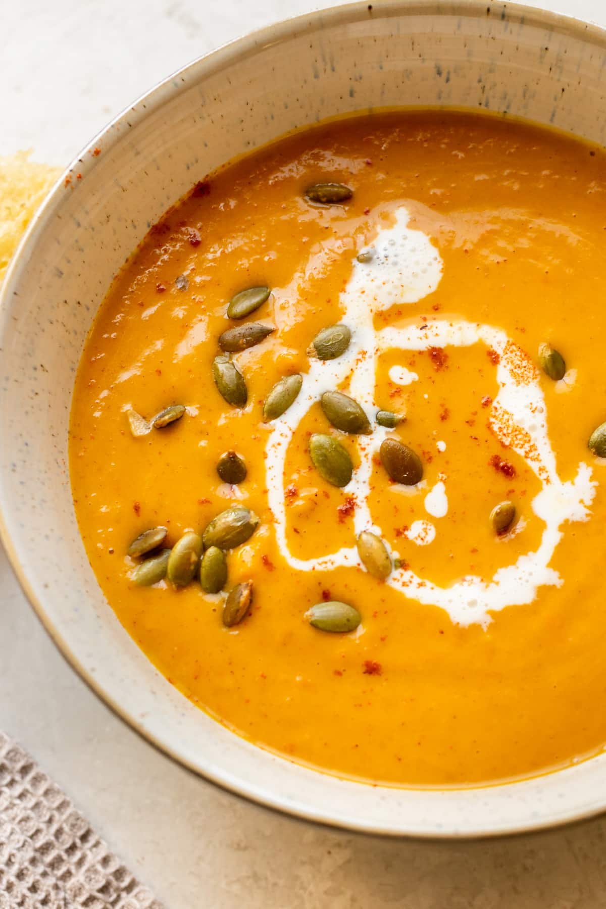 squash soup in a bowl topped with pepitas, cream, and paprika.