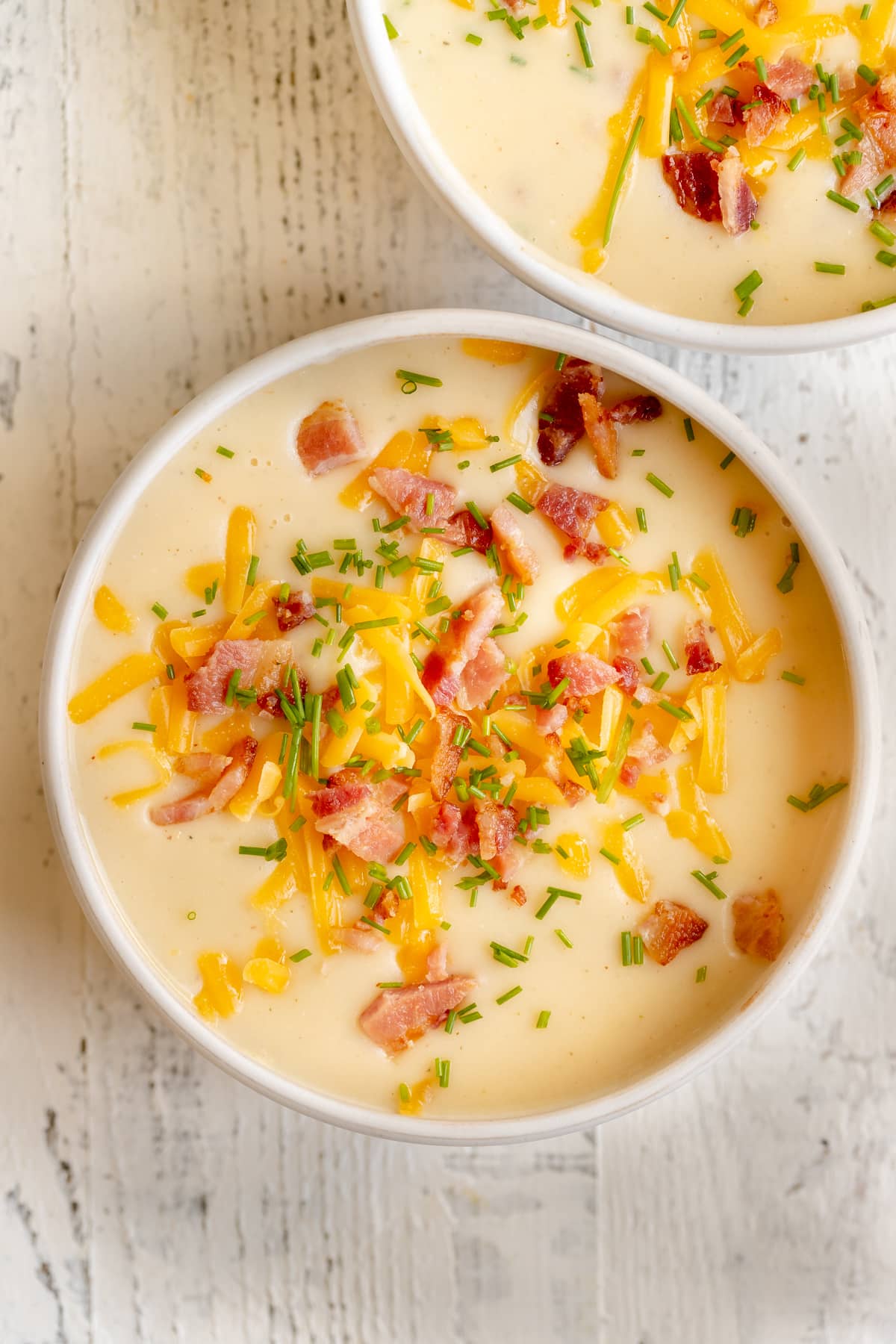 baked potato soup in a white bowl garnished with bacon, cheese and chives. 