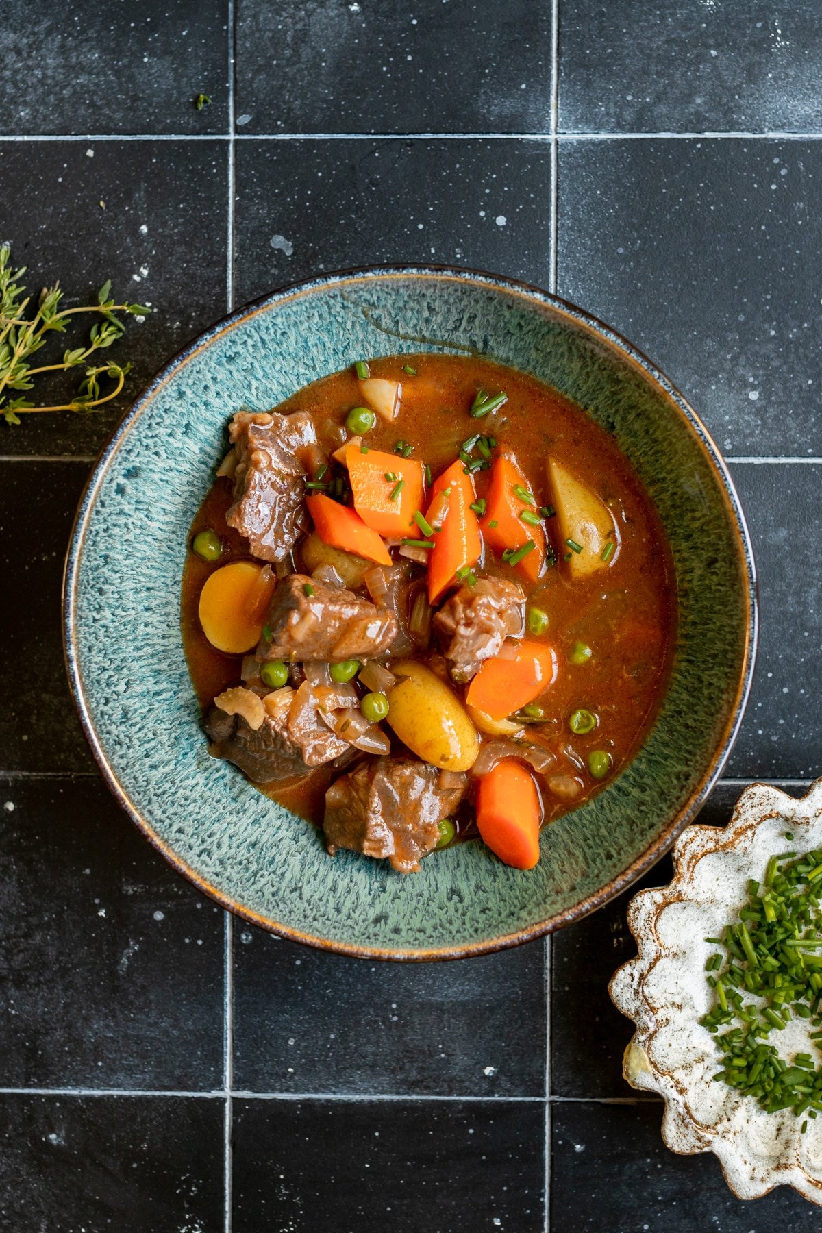 stew made with beef, potatoes and carrots in a blue bowl garnished with fresh chopped chives.