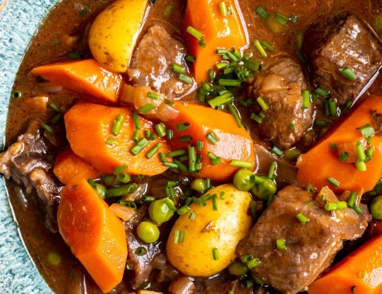 stew made with beef, potatoes and carrots in a blue bowl garnished with fresh chopped chives.