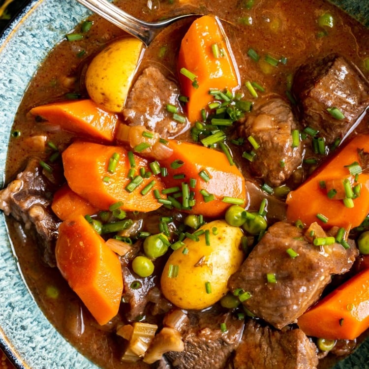 stew made with beef, potatoes and carrots in a blue bowl garnished with fresh chopped chives.