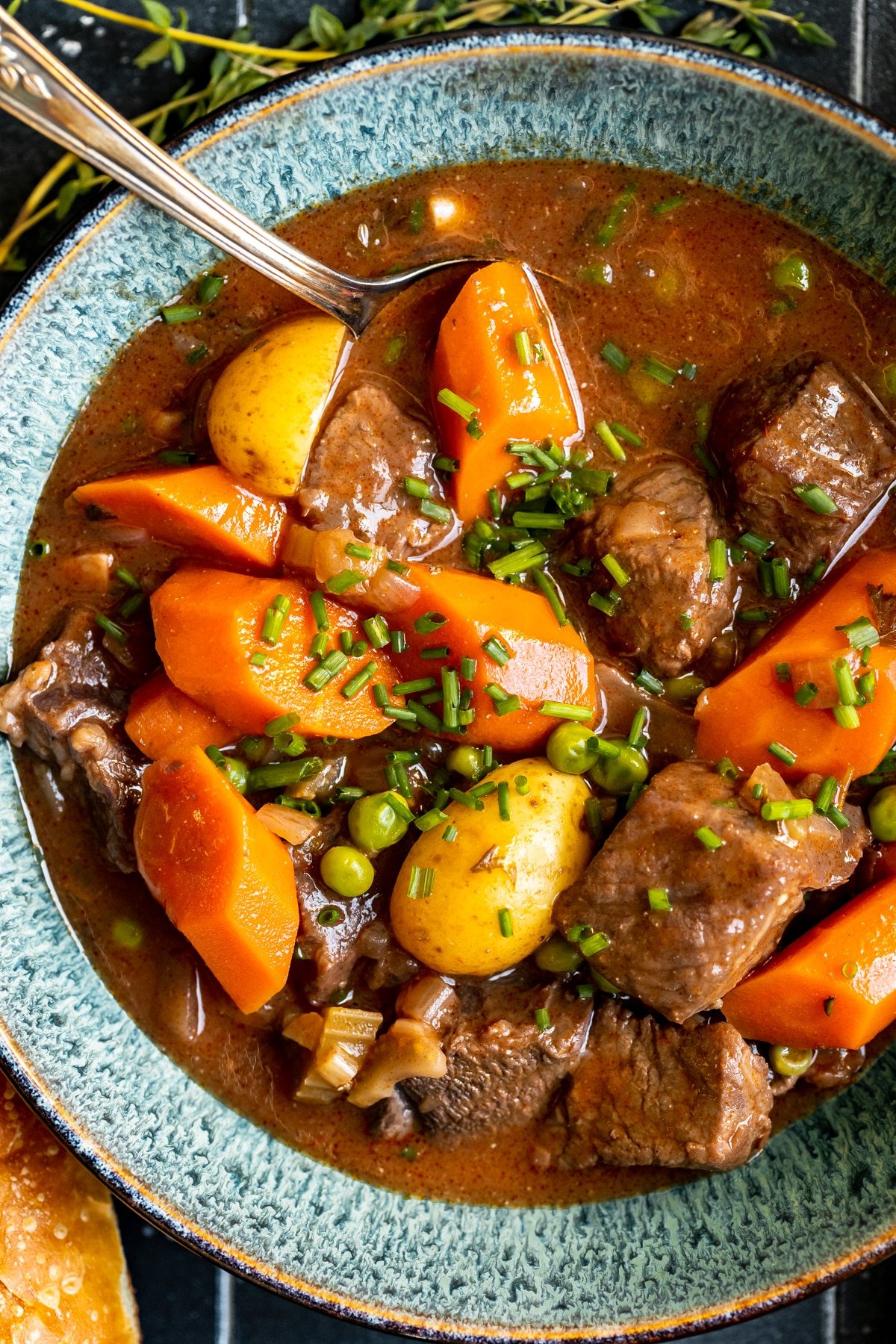 stew made with beef, potatoes and carrots in a blue bowl garnished with fresh chopped chives.