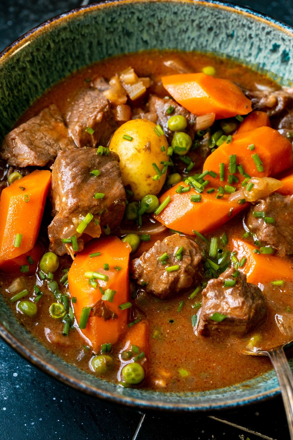 stew made with beef, potatoes and carrots in a blue bowl garnished with fresh chopped chives.