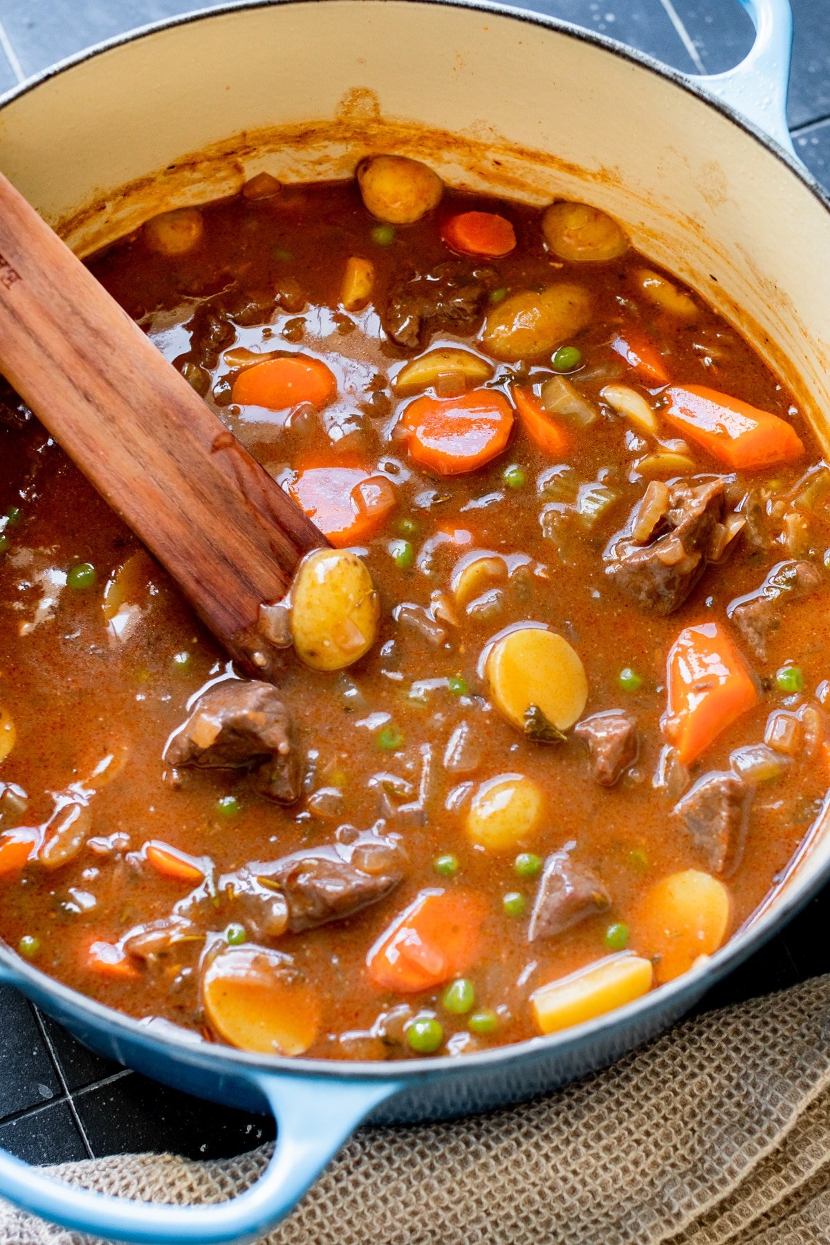 stew made with beef, potatoes and carrots in a blue Dutch oven with a wooden spoon.