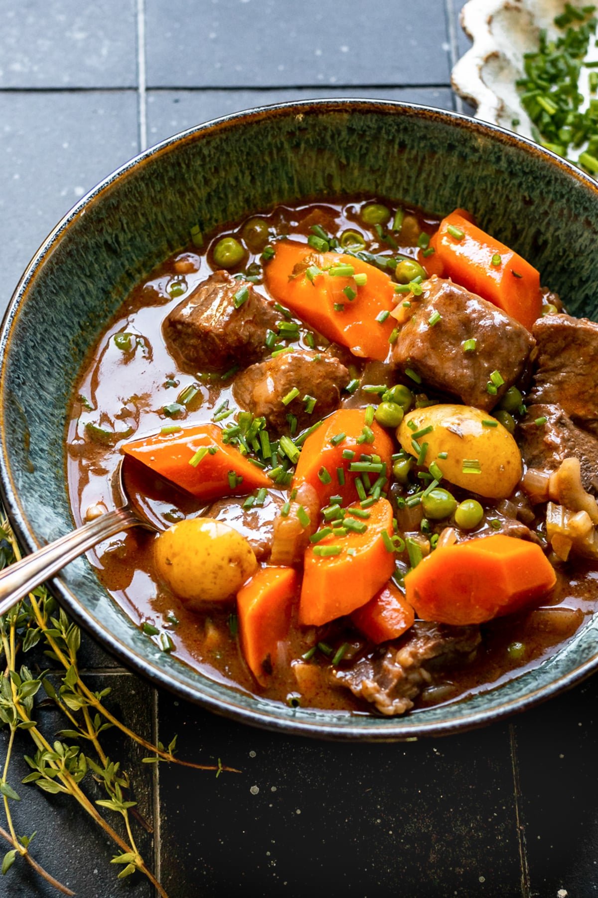 stew made with beef, potatoes and carrots in a blue bowl garnished with fresh chopped chives.