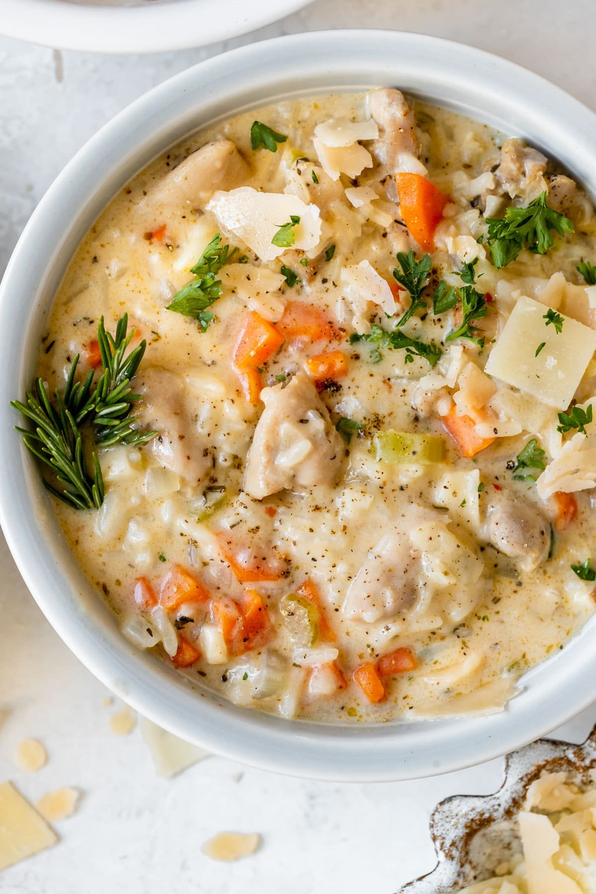 chicken rice soup in a bowl garnished with parmesan cheese, black pepper and fresh parsley.