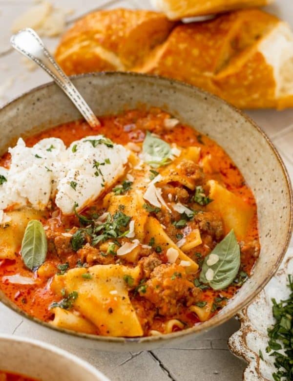 soup made with lasagna noodles in a bowl garnished with ricotta, parsley, basil and parmesan cheese.