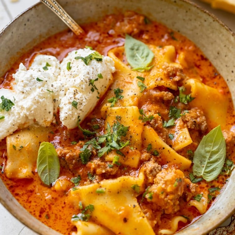 soup made with lasagna noodles in a bowl garnished with ricotta, parsley, basil and parmesan cheese.