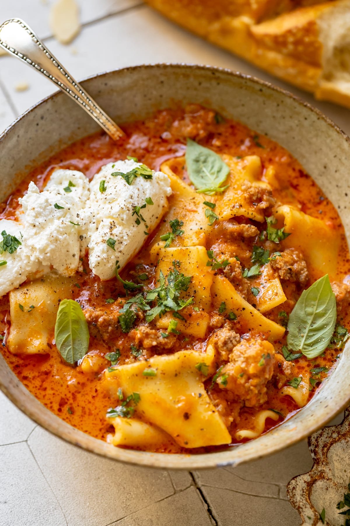 soup made with lasagna noodles in a bowl garnished with ricotta, parsley, basil and parmesan cheese.