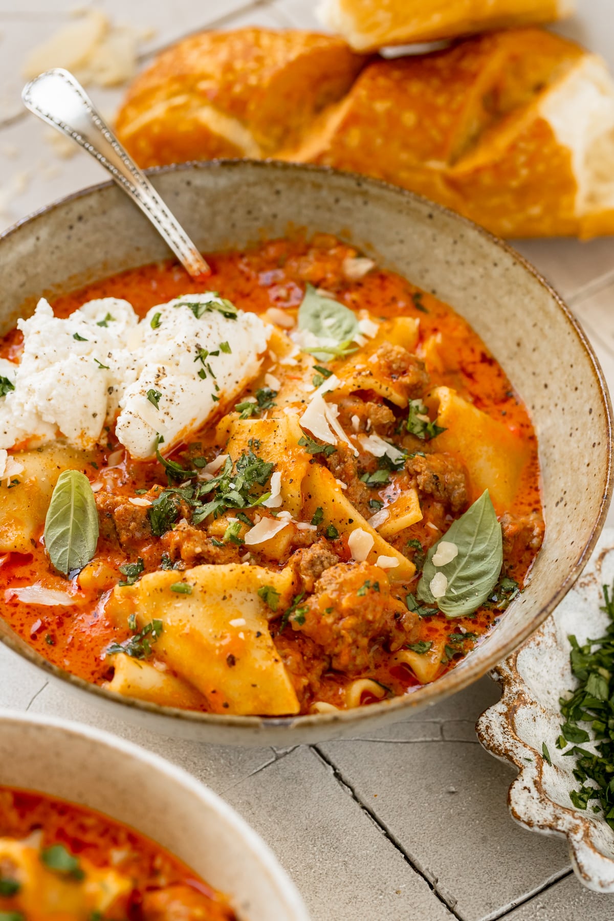 soup made with lasagna noodles in a bowl garnished with ricotta, parsley, basil and parmesan cheese.