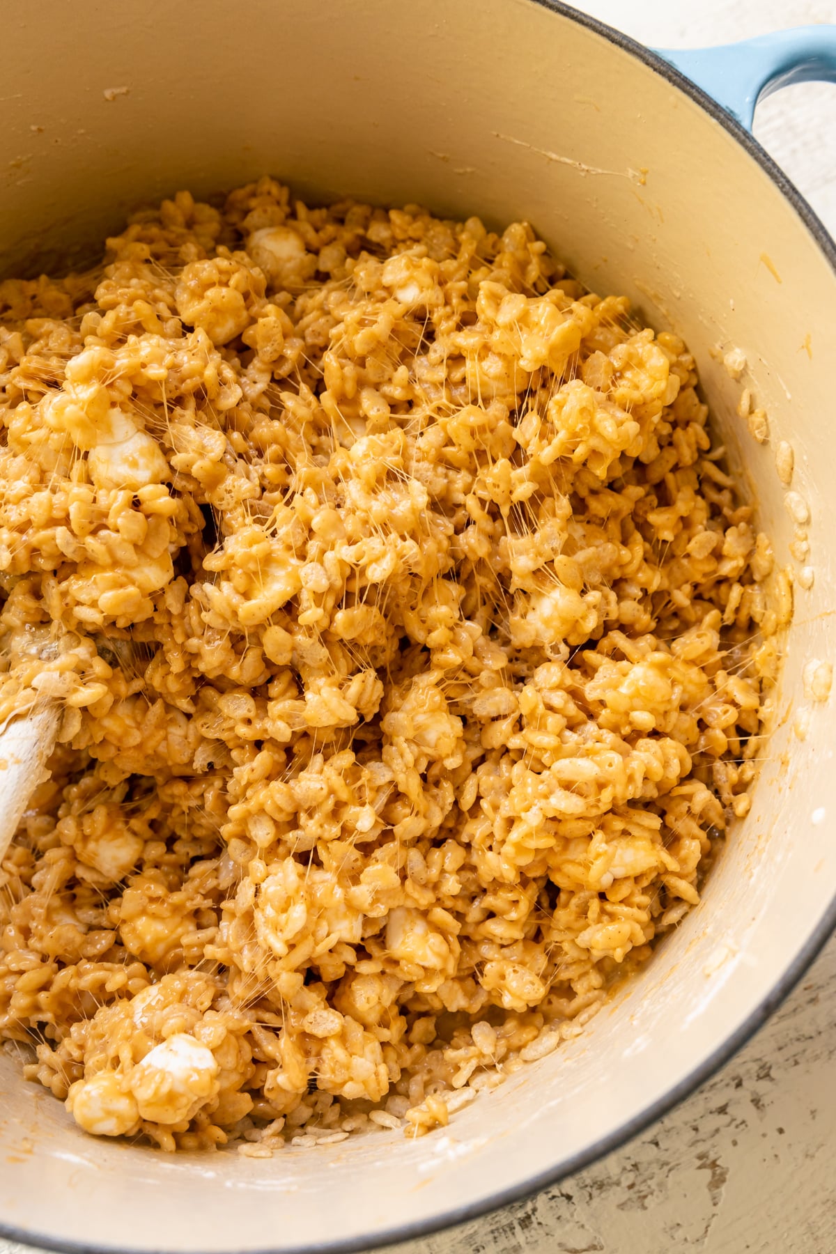 a wooden spoon stirring rice krispies in a dutch oven. 