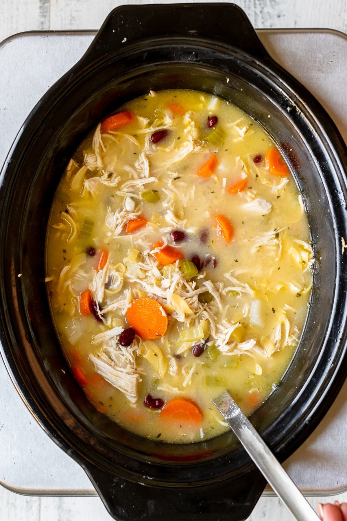 noodle soup made with chicken and vegetables in a black crockpot. 