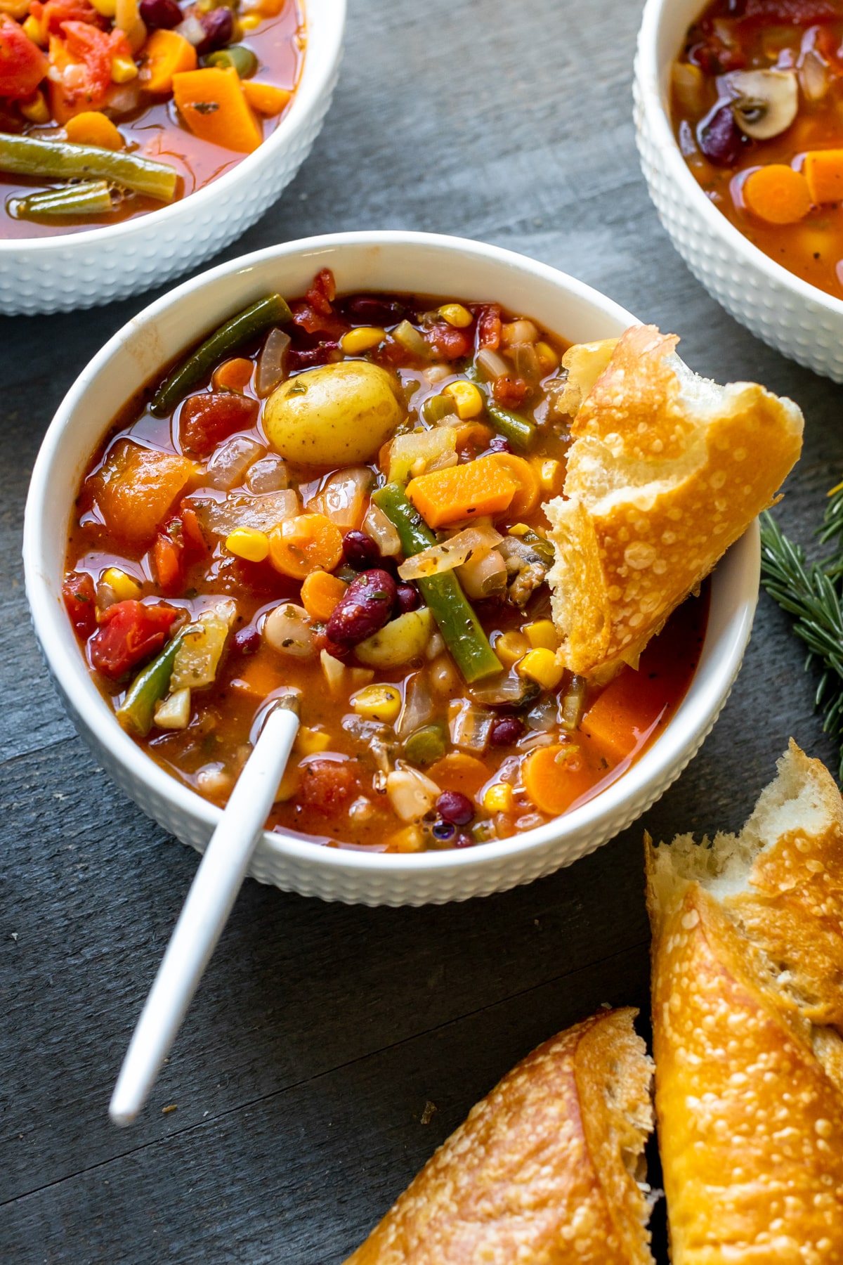 vegetable soup in a white bowl with crusty bread on the side. 