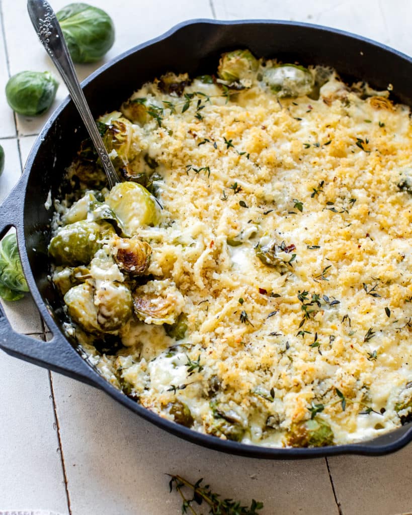 Brussel sprouts in a cast iron skillet covered in a cheese sauce and panko breadcrumbs and fresh thyme. 