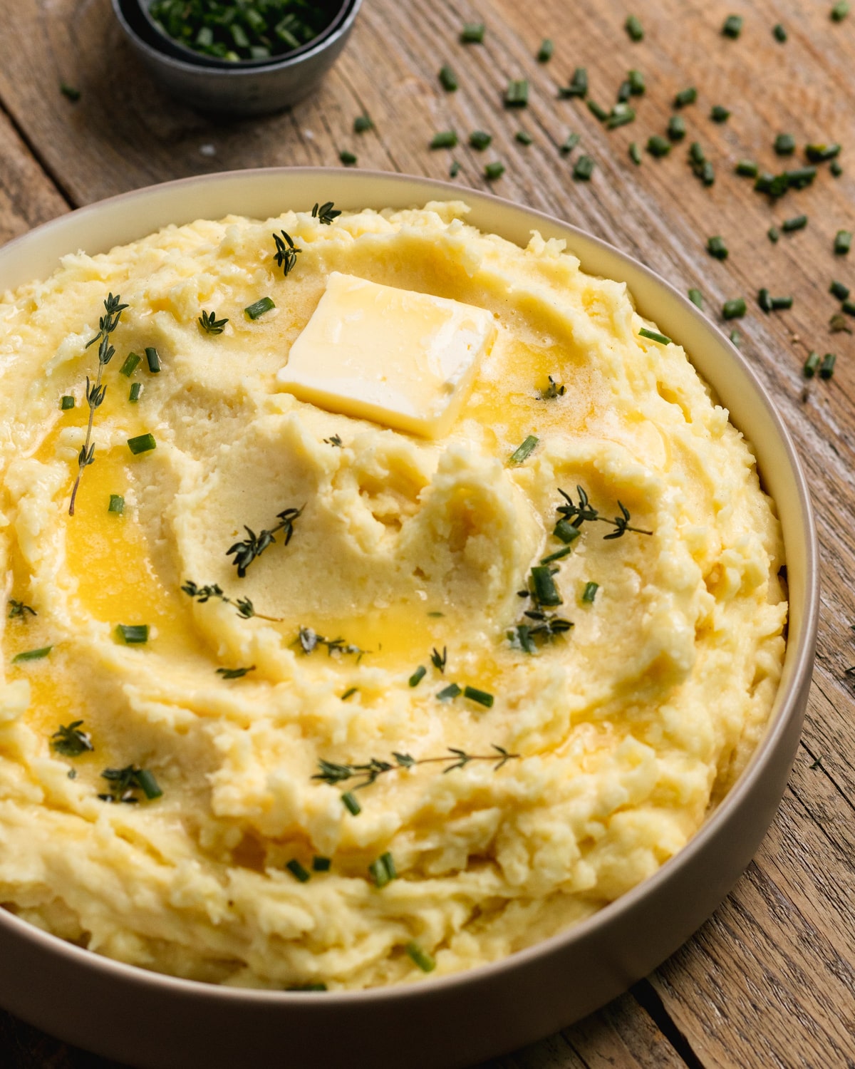 potatoes in a bowl garnished with butter, thyme and chives. 