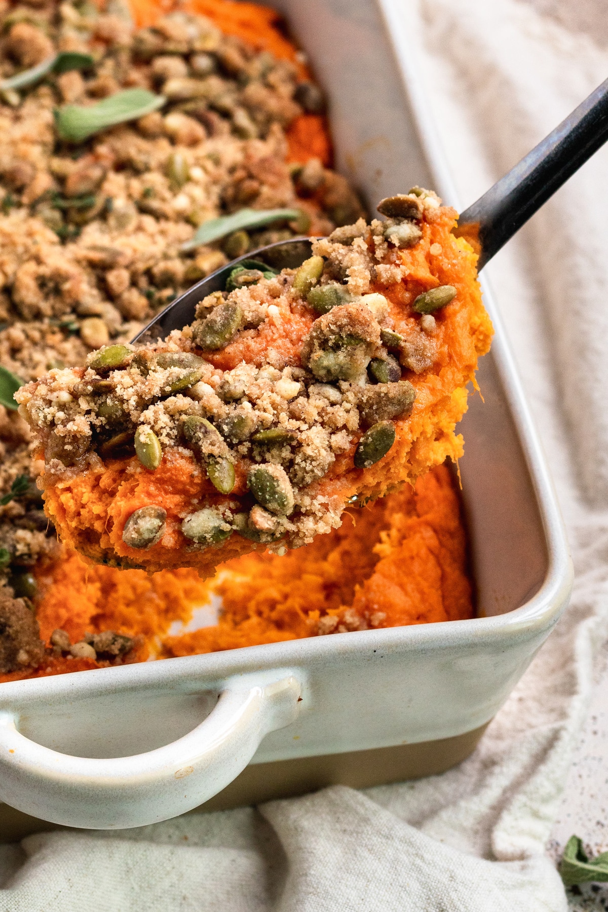 am up close image of a black spoon scooping out sweet potato casserole from a white casserole dish.