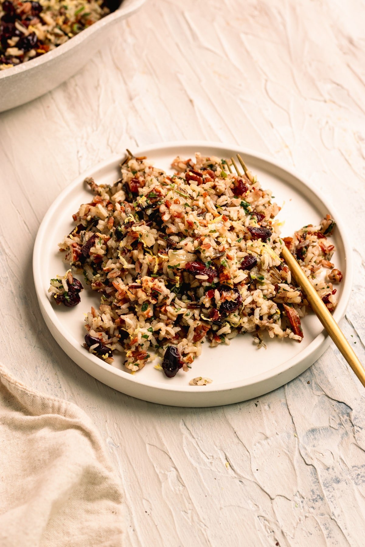 rice pilaf made with a wild rice blend on a white plate with a gold fork. 
