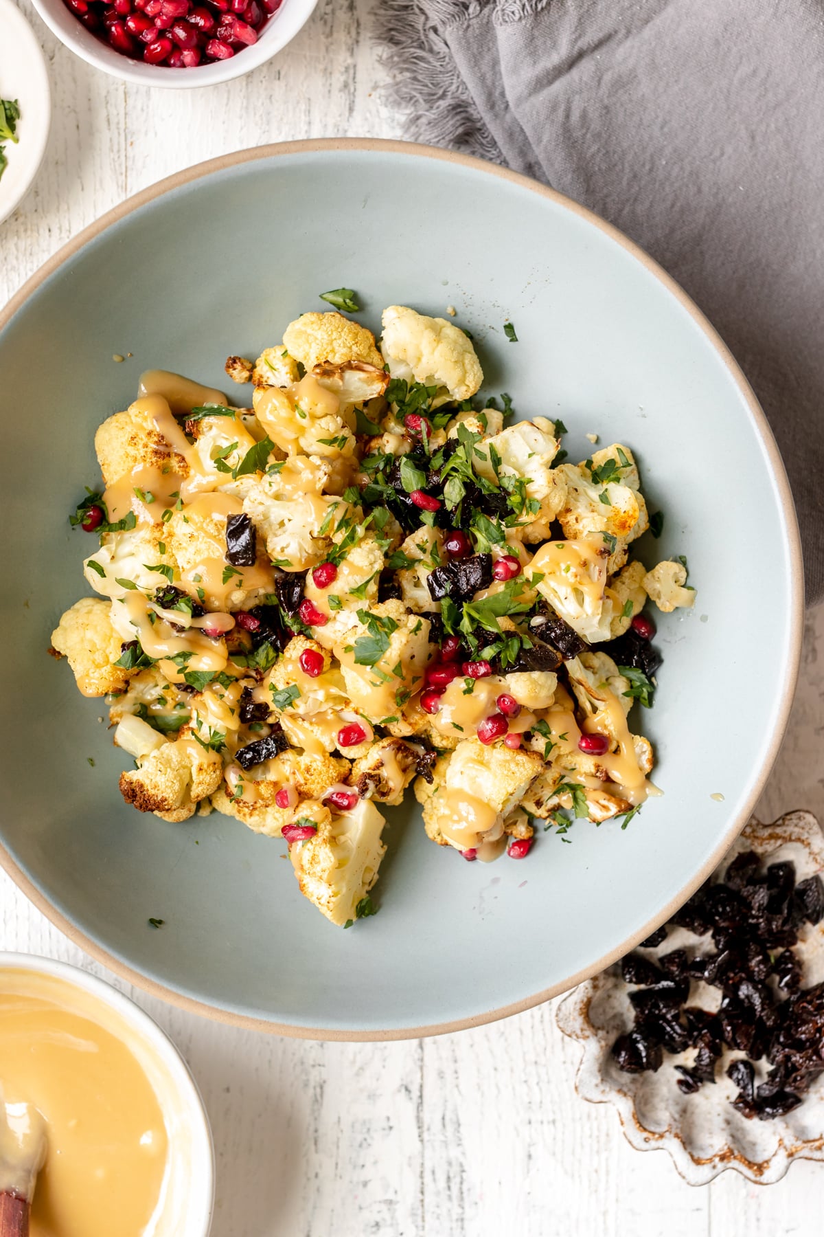 cauliflower in a blue bowl garnished with parsley, pomegranates and prunes. 