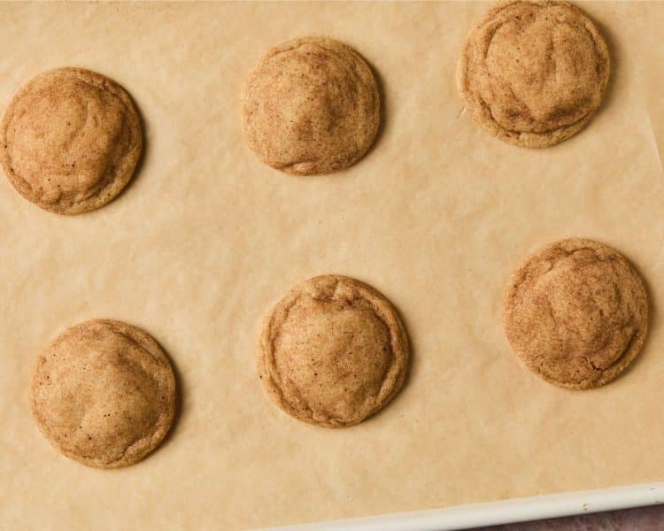 Six baked cookies with cinnamon sugar topping on brown parchment paper.