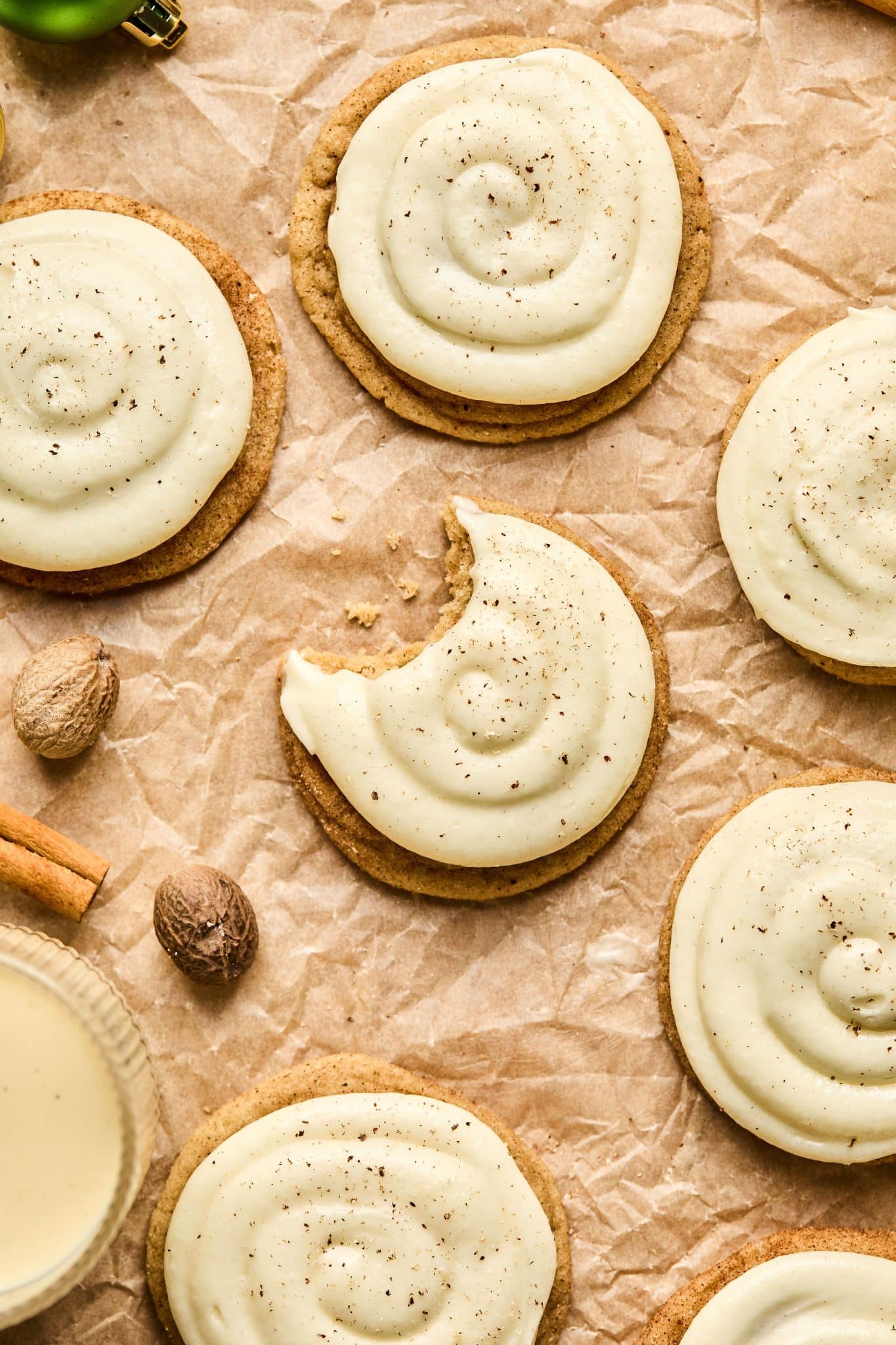 Multiple eggnog cookies with cream cheese frosting featuring one in center with a bite taken out.