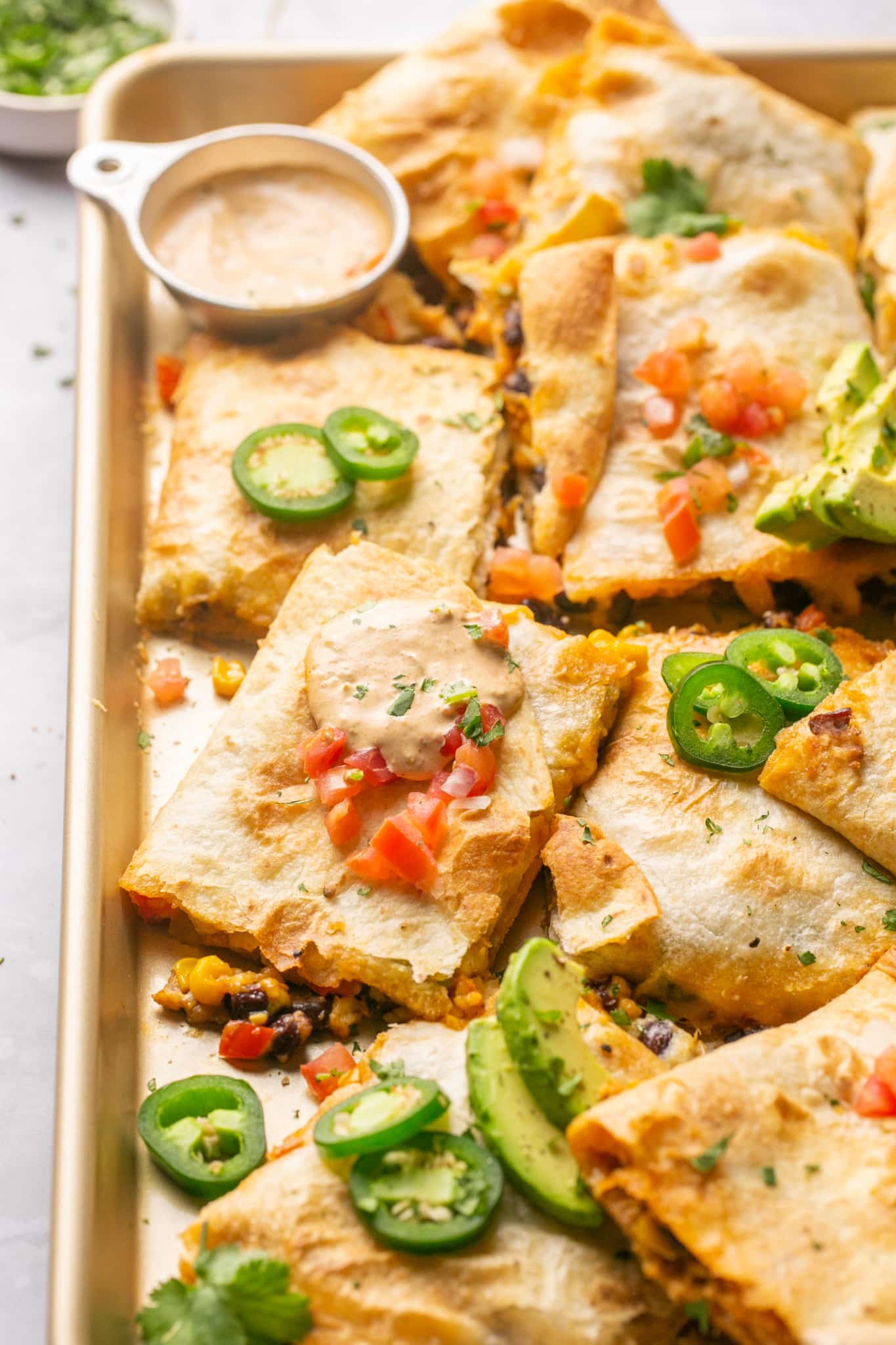 quesadillas on a sheet pan with jalapenos and avocado garnished on top.