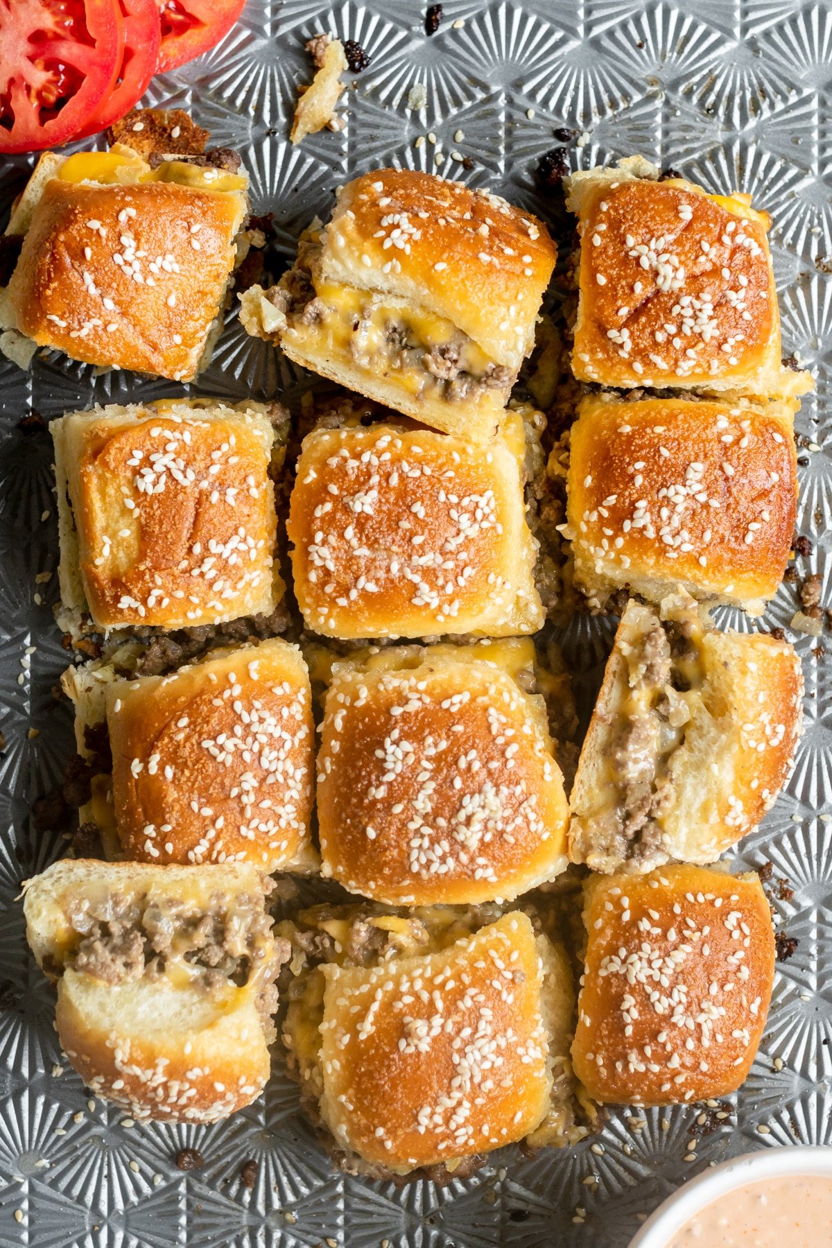 cheeseburger sliders topped with sesame cheese on a sheet pan. 