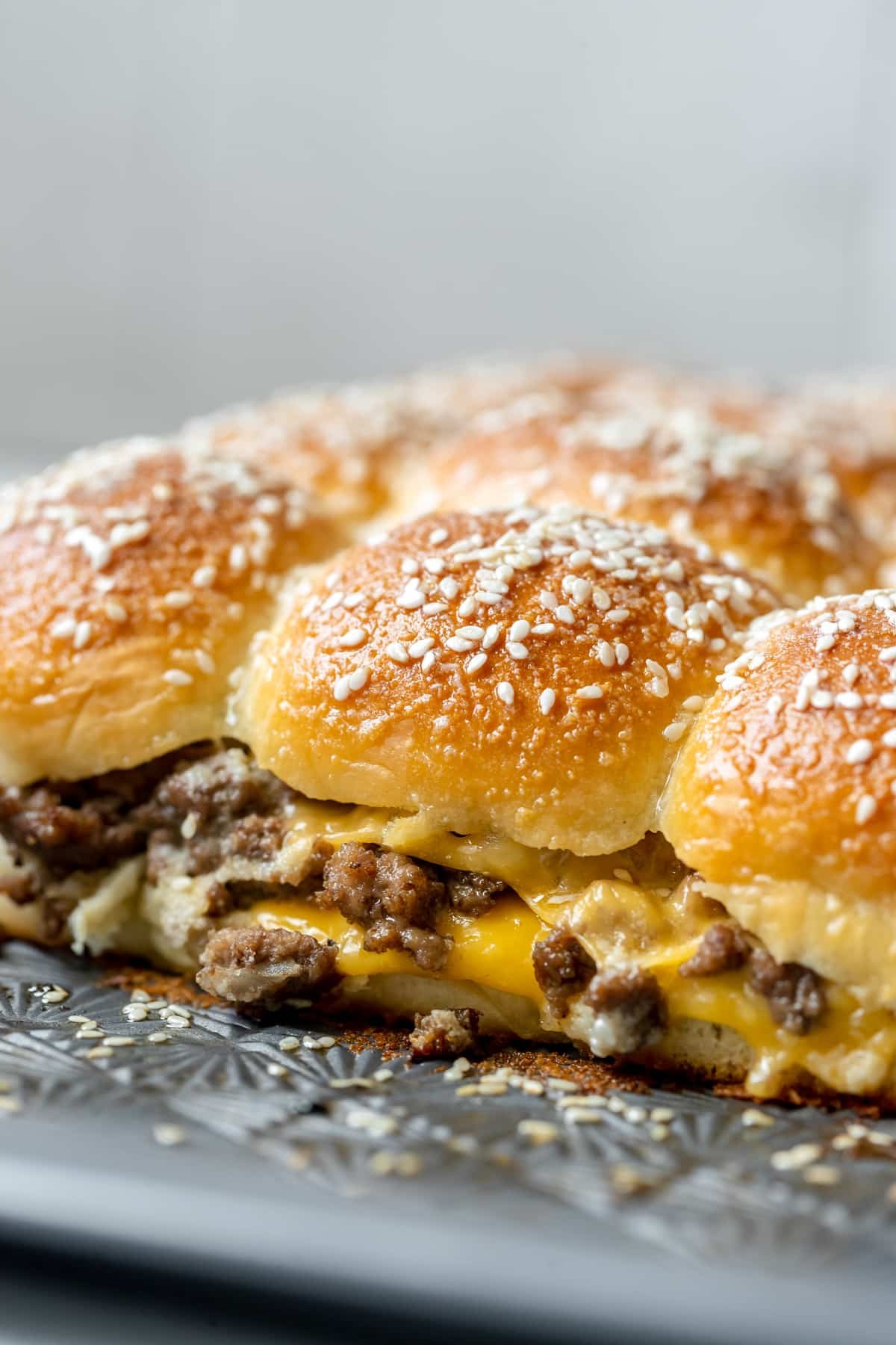 cheeseburger sliders topped with sesame cheese on a sheet pan. 