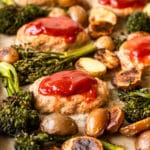 mini meatloaves topped with ketchen on a sheet pan surrounded by roasted broccoli and potatoes