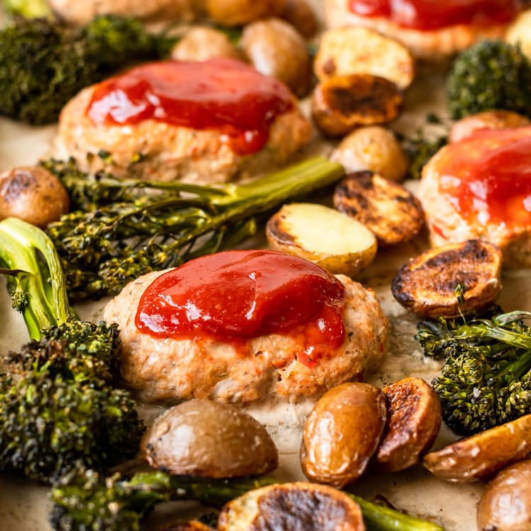 mini meatloaves topped with ketchen on a sheet pan surrounded by roasted broccoli and potatoes