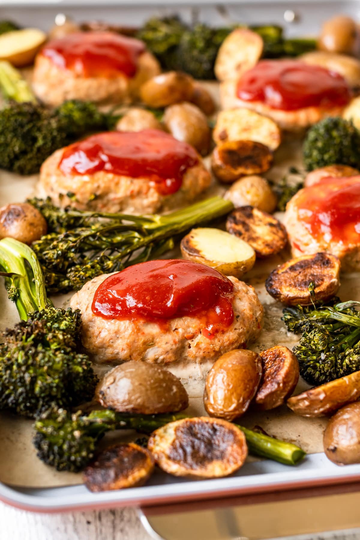 mini meatloaves topped with ketchen on a sheet pan surrounded by roasted broccoli and potatoes