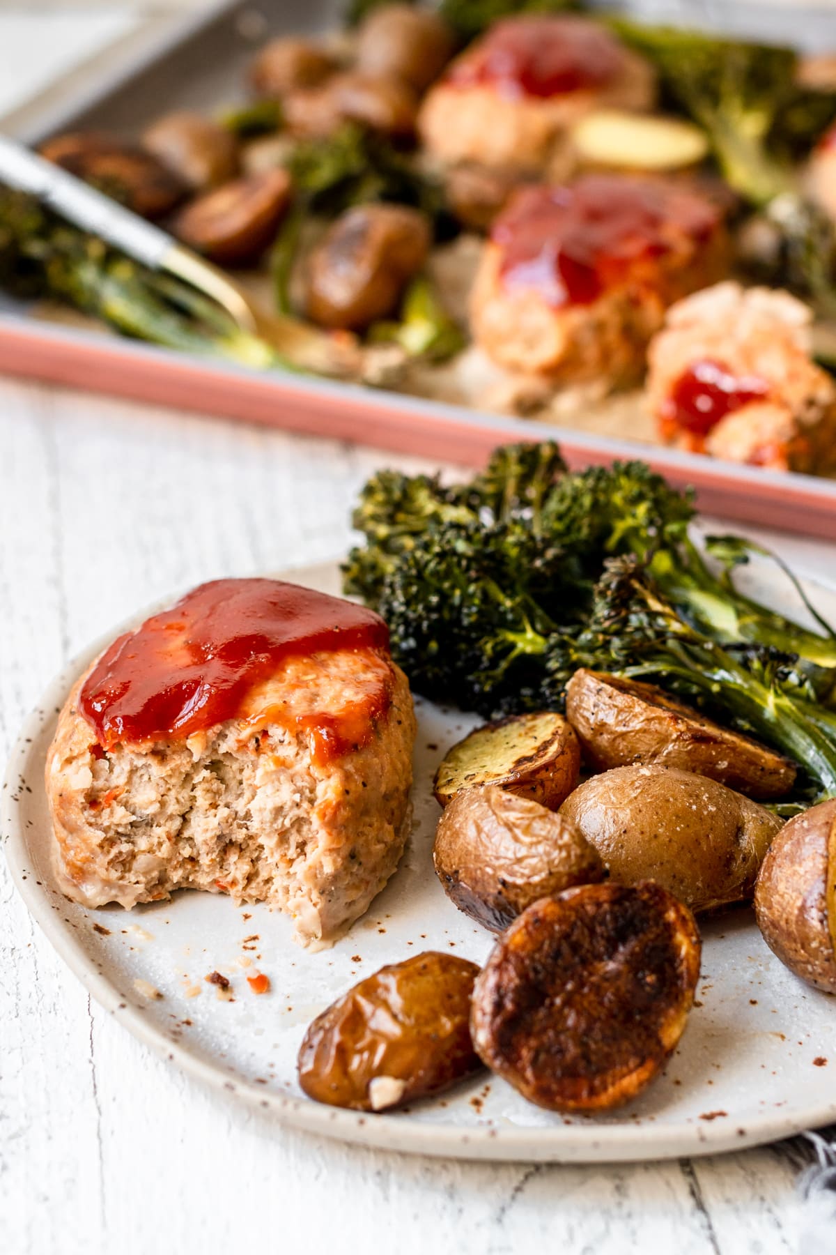 an up close image of a bite taken out of a meatloaf on a plate with potatoes and broccoli. 