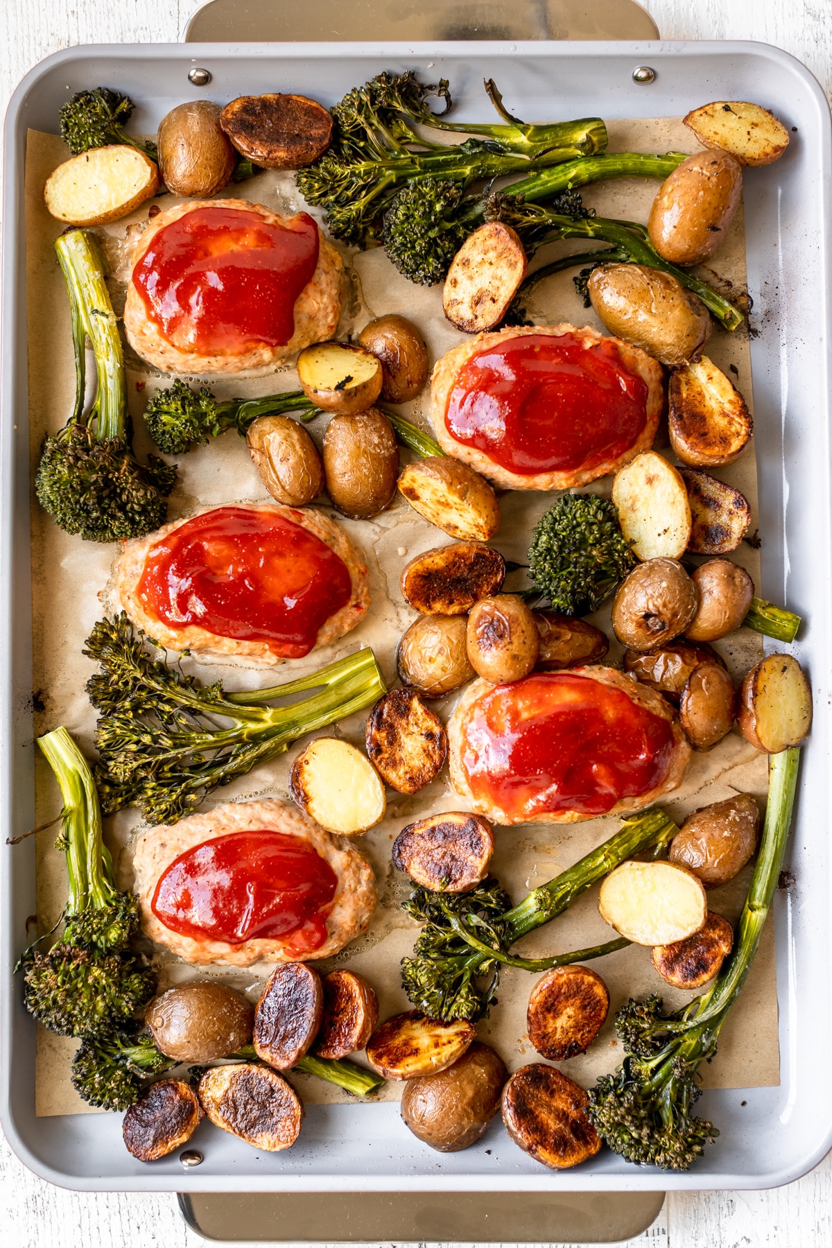 a sheet pan dinner made with ground turkey meatloaves, broccolini and roasted potatoes. 