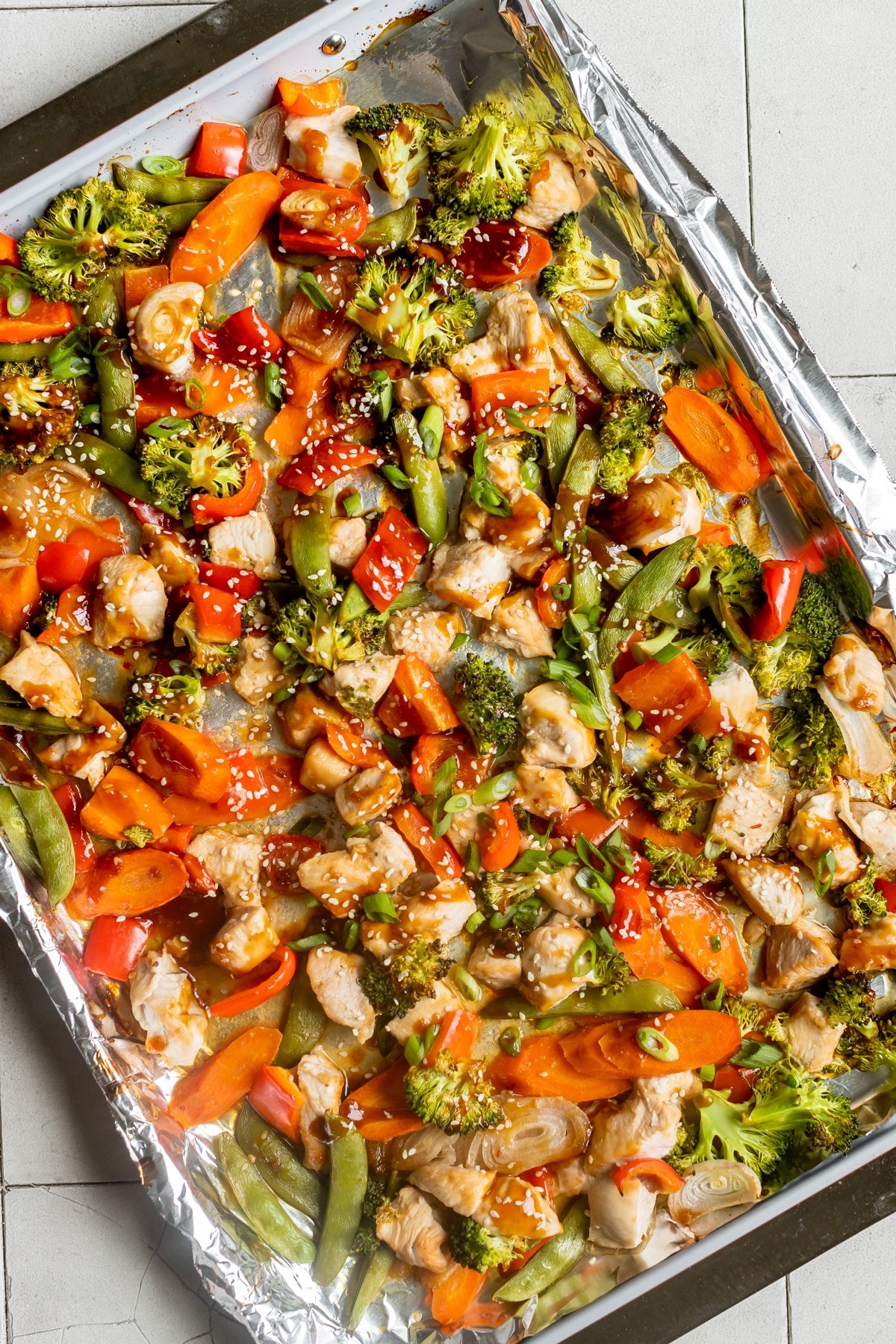chicken and veggies on a sheet pan garnished with sesame seeds and green onions. 