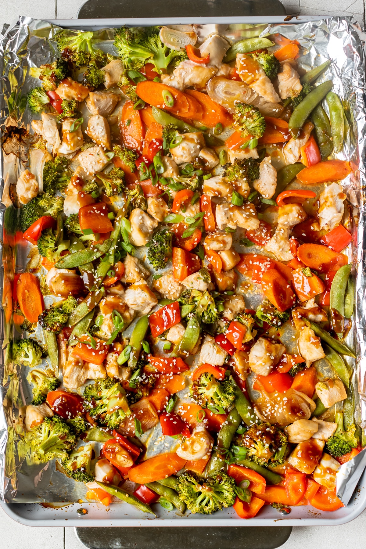 chicken and vegetables on a sheet pan lined with foil with sauce drizzled over the top. 