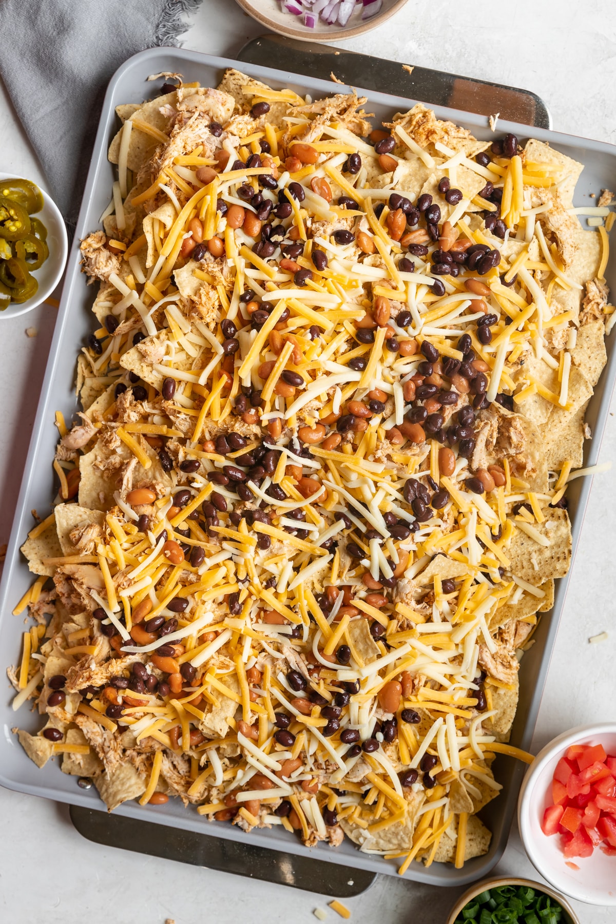 chips, beans, chicken and cheese layered on a sheet pan. 