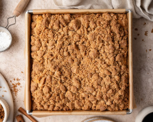 Hand sprinkling crumb topping over the cake batter; next frame shows the pan fully covered with an even layer of streusel.