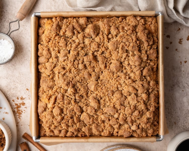 Hand sprinkling crumb topping over the cake batter; next frame shows the pan fully covered with an even layer of streusel.