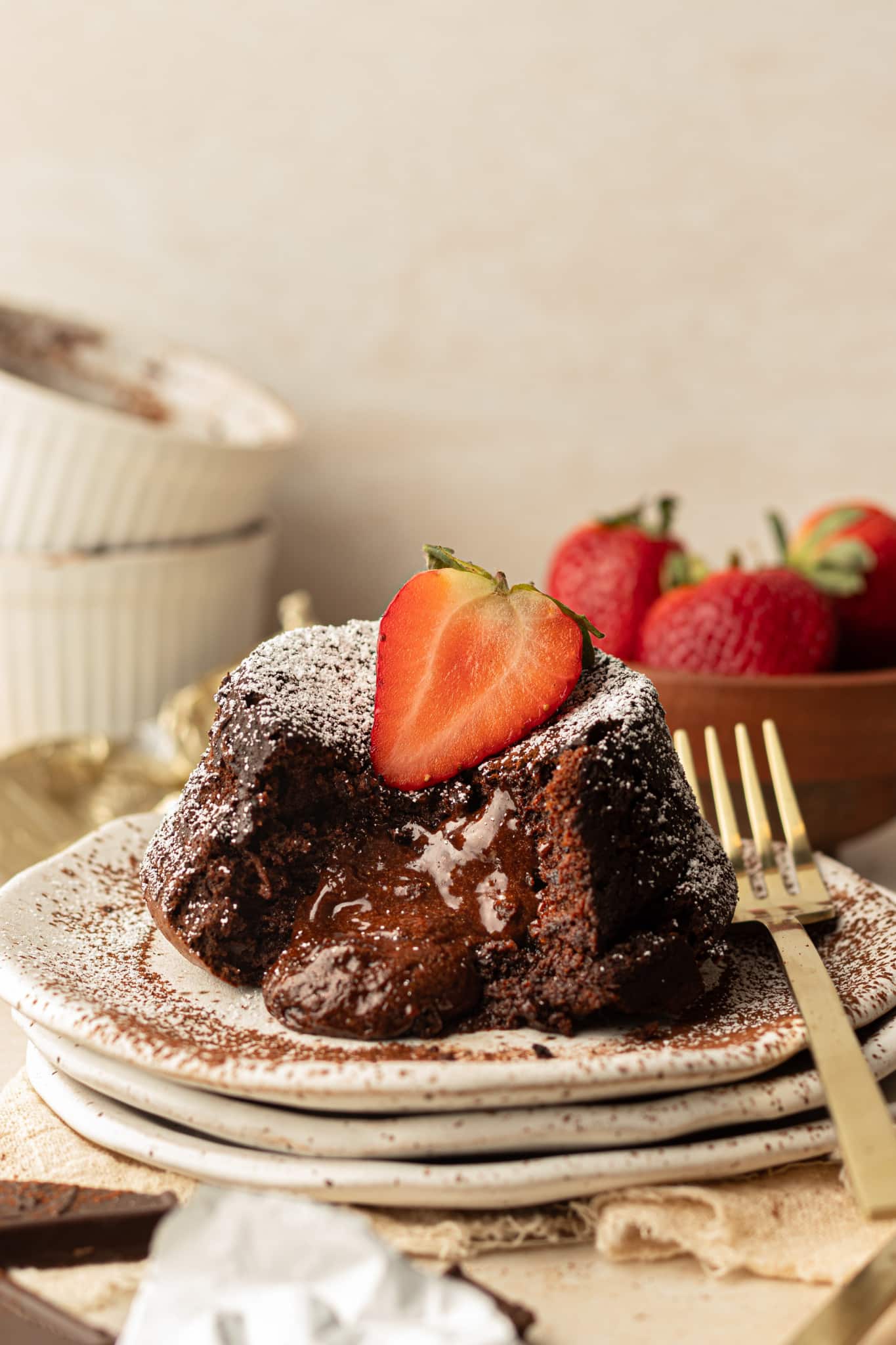 an image of chocolate molten cakes with a gold fork on the plate and a strawberry on top. 