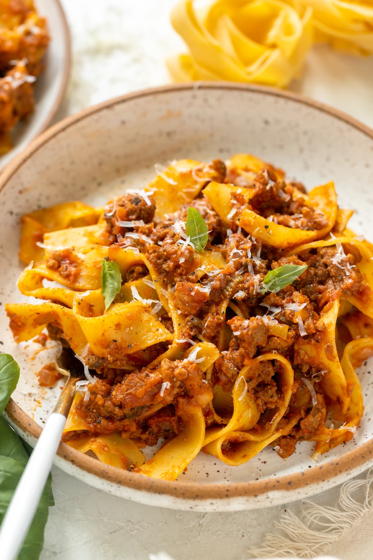 pasta in a white bowl with meat sauce garnished with parmesan cheese. 