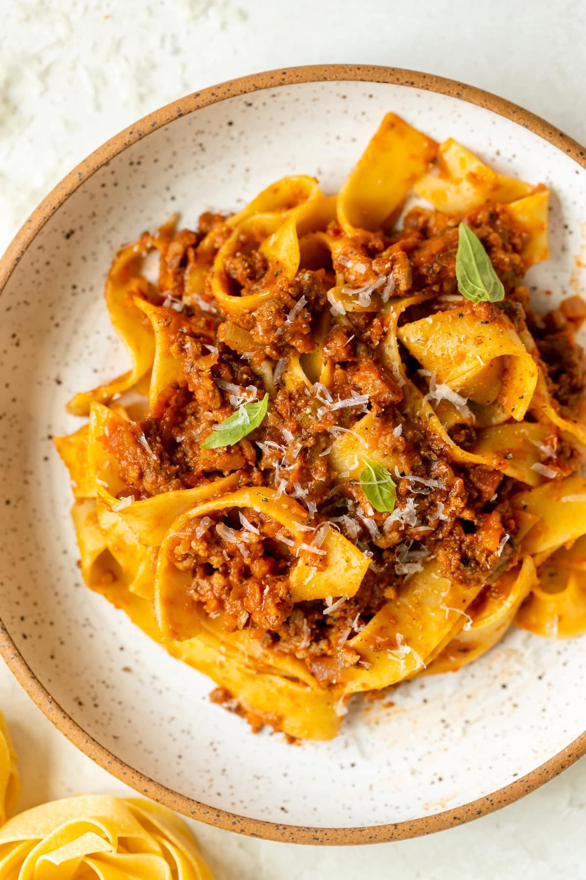 pasta in a white bowl with meat sauce garnished with parmesan cheese. 