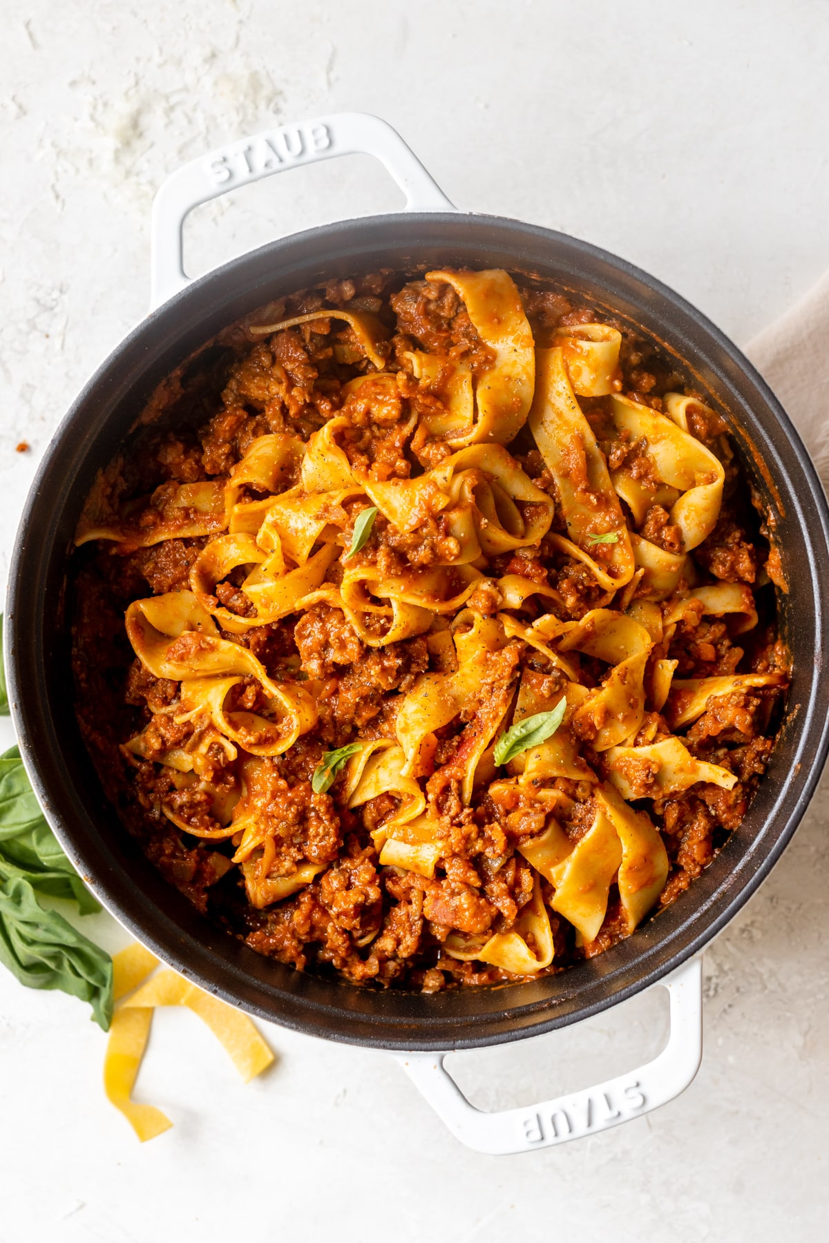 bolognese sauce swirled in cooked pappardelle pasta noodles with a white dutch oven. 