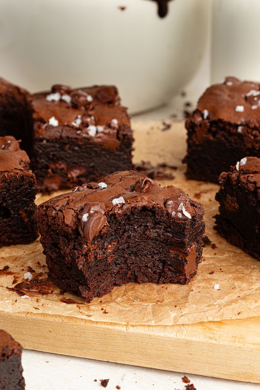 Close-up of a thick brownie with a bite taken out, revealing a dense and fudgy texture with melty chocolate chunks. Set on parchment paper with other brownies nearby.