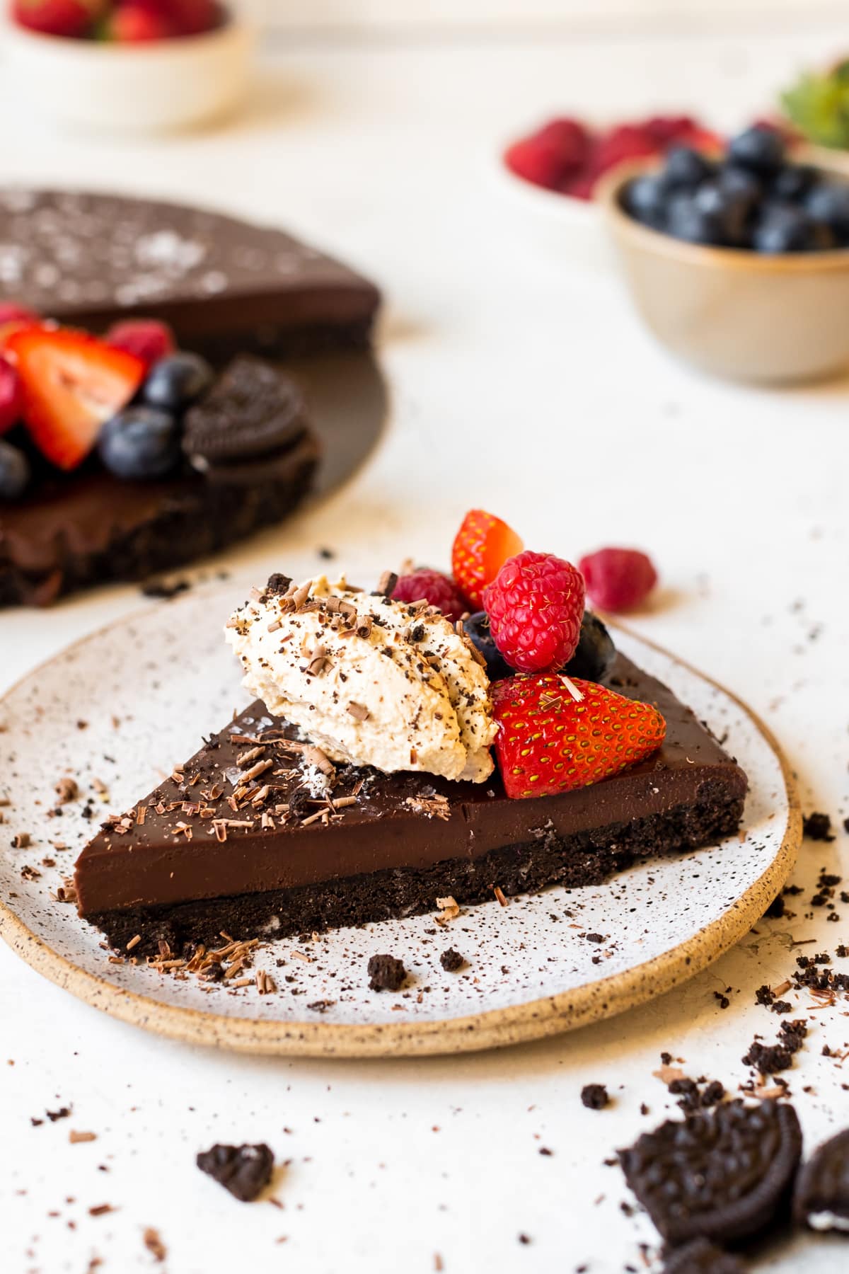 a slice of chocolate tart on a plate topped with whipped cream and fresh berries. 