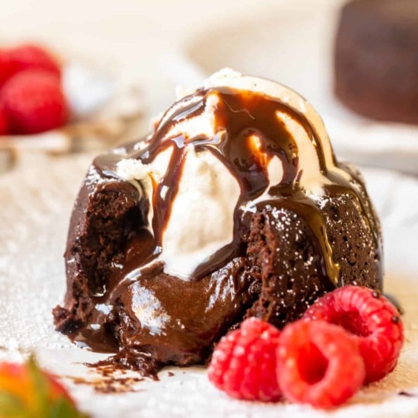 individual chocolate cake with melted chocolate pouring out the middle topped with vanilla ice cream and chocolate syrup.