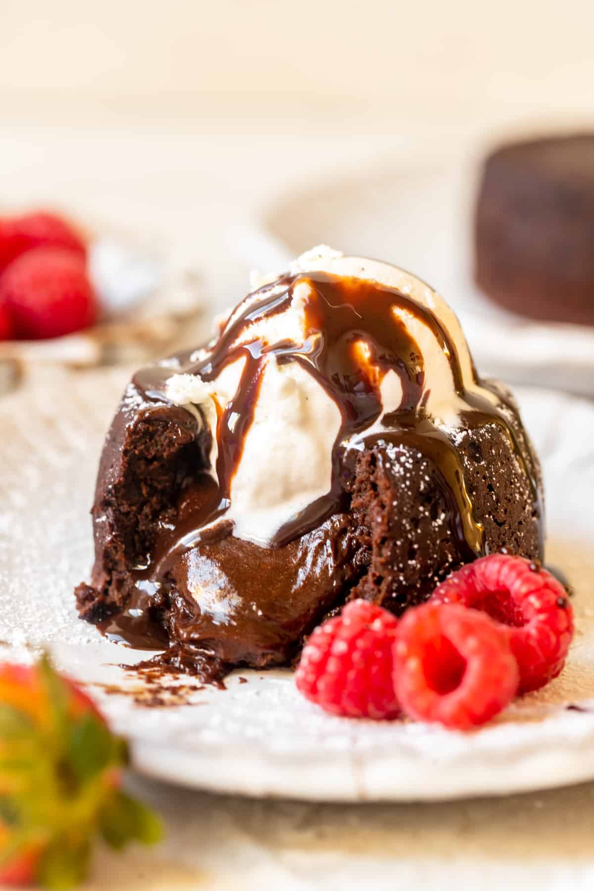 individual chocolate cake with melted chocolate pouring out the middle topped with vanilla ice cream and chocolate syrup.