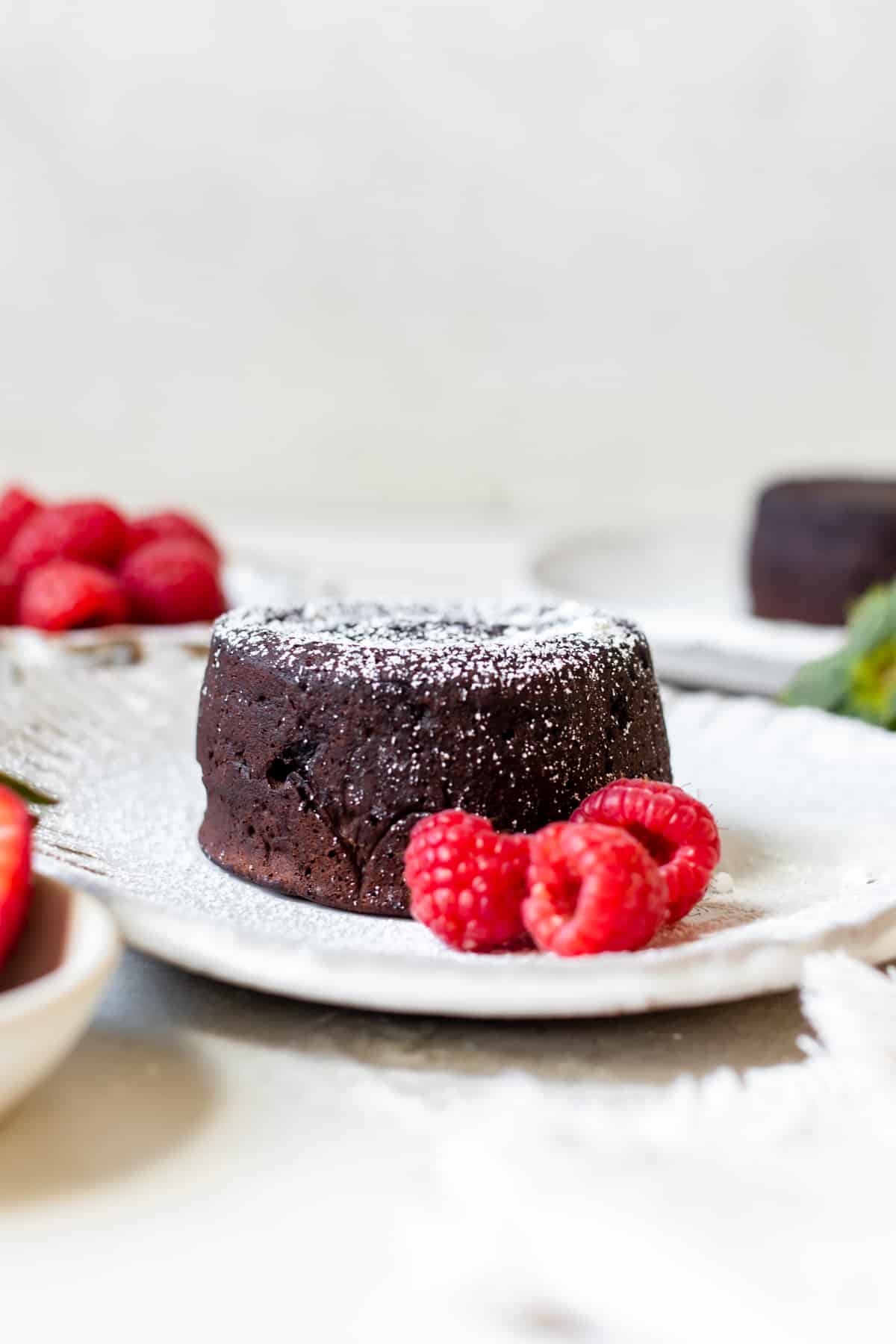 molten cake on a white plate with raspberries garnished with powdered sugar 