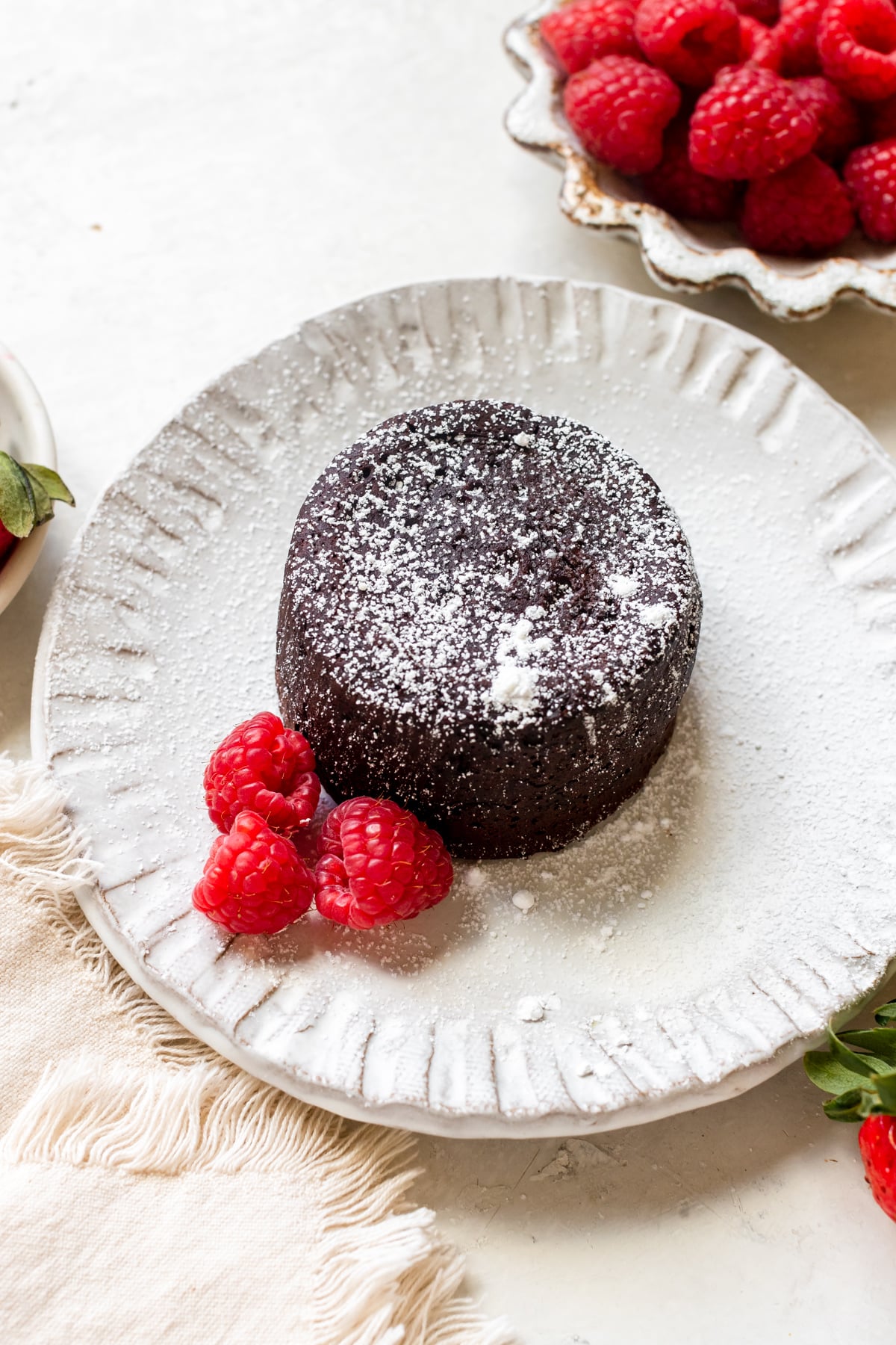 molten cake on a white plate with raspberries garnished with powdered sugar 